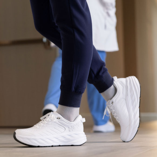 White sneakers worn with navy pants and a white jacket on a wooden floor.