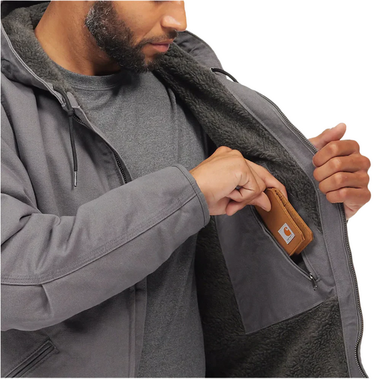 Carhartt Men's Relaxed Fit Washed Duck Sherpa Lined Jacket - Gravel on a male model on a white background. Zoomed into  him putting a wallet in an interior zip up pocket.