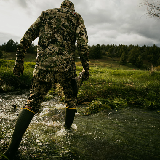Person in camouflage gear walking through a stream in a forested area