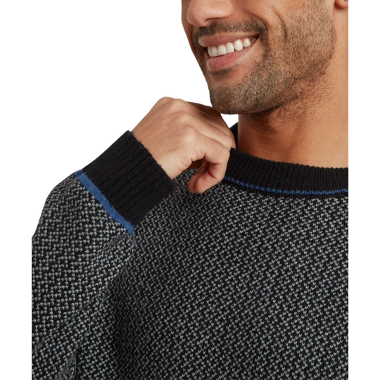 Close-up of a man wearing a textured knit crewneck sweater in black, gray, and white, with a thin blue stripe detail at the collar.