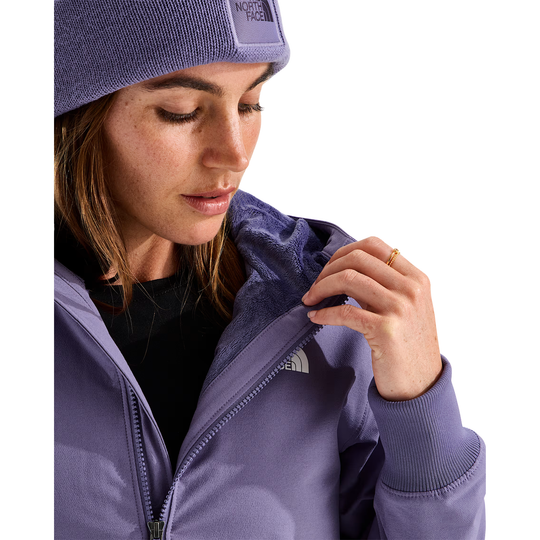 A close-up of a woman wearing a lavender-purple The North Face zip-up jacket and matching beanie, looking down while adjusting the collar of the jacket.