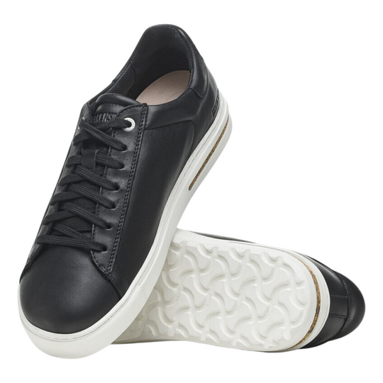 Black low-top sneakers with laces, a white platform sole, and a cork accent in the heel. On a plain white background. 