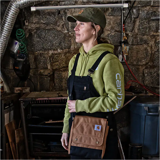 Person wearing a green hoodie with Carhartt logo and brown work pants in a workshop.