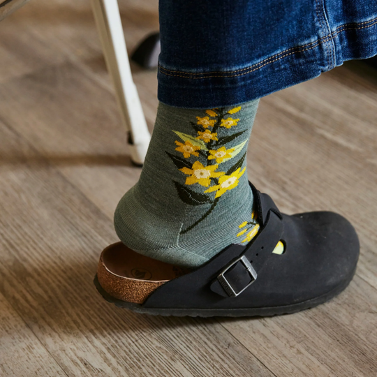 Black clog sandal worn with olive green floral socks and blue jeans