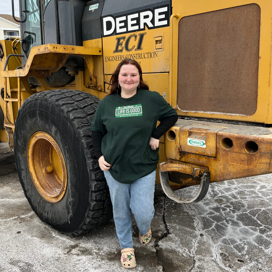 Person standing next to a large yellow construction vehicle with 'Deere' branding.