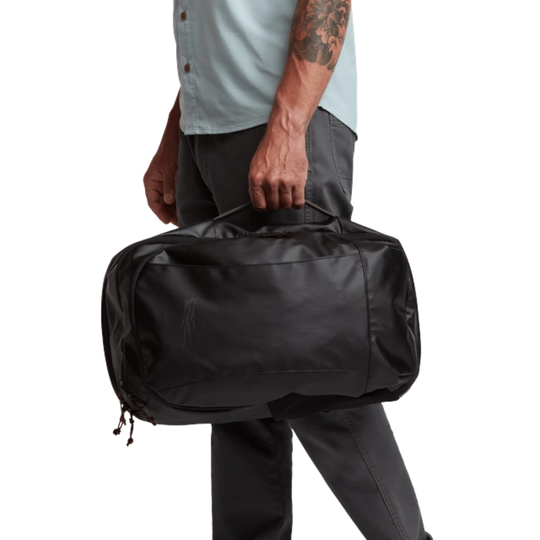 Person holding a black duffel bag against a white background