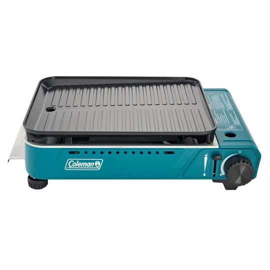 Portable teal tabletop grill with a black ridged cooking grate and visible Coleman logo