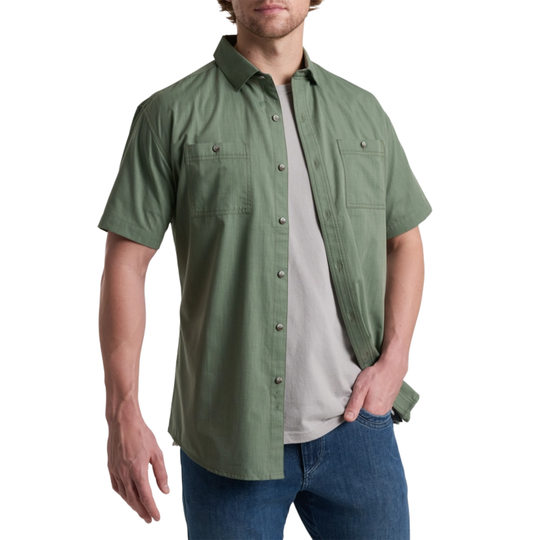 Man wearing a green short-sleeve shirt over a gray t-shirt with blue jeans on a white background