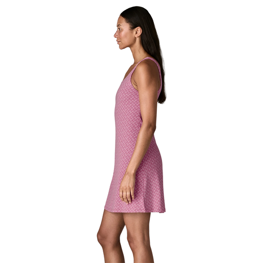 A woman shown in side profile wearing a sleeveless pink dress with a small repeating geometric pattern, photographed against a plain white studio background.