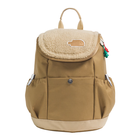 A tan canvas backpack with a beige sherpa fleece flap, featuring a front pocket with a snap button, side pockets, top carry handles, and small colorful hanging charms on the right side.