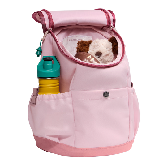 A light pink diaper bag backpack shown on a white background, filled with a yellow and teal water bottle, a brown stuffed animal, and a white plush toy.