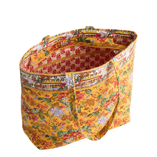 A large fabric tote bag with a yellow background and a detailed multicolor toile-style print featuring flowers, animals, and buildings, shown on a plain white background.