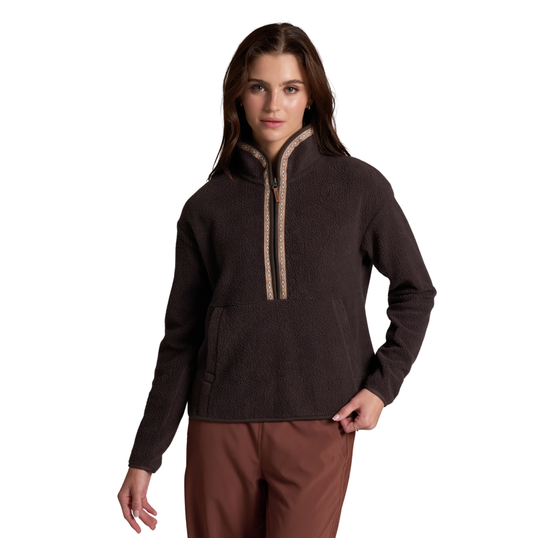 A woman modeling a dark brown fleece pullover with a quarter-zip neckline featuring a beige patterned trim, paired with brown pants, against a solid white background.