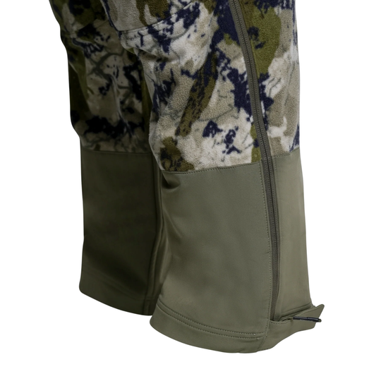 Close-up of the lower legs of camouflage hunting pants with olive green bifold leg extensions or gaiters, shown on a plain white background.