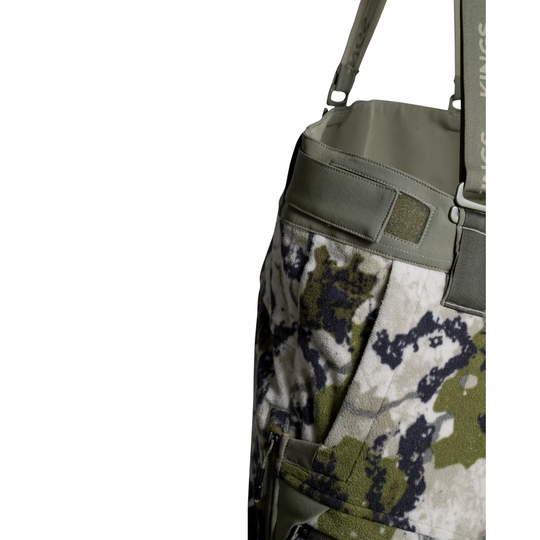Close-up of a tactical bag or duffel bag featuring a digital camouflage pattern in olive green, beige, and dark gray, with a solid olive green strap and buckle details, set against a plain white background.