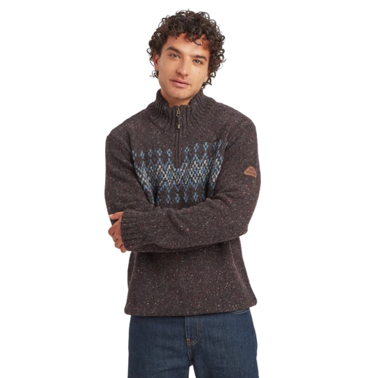 A man wearing a dark brown heathered quarter-zip sweater with a blue and gray geometric pattern across the chest, paired with blue jeans, against a plain white background.