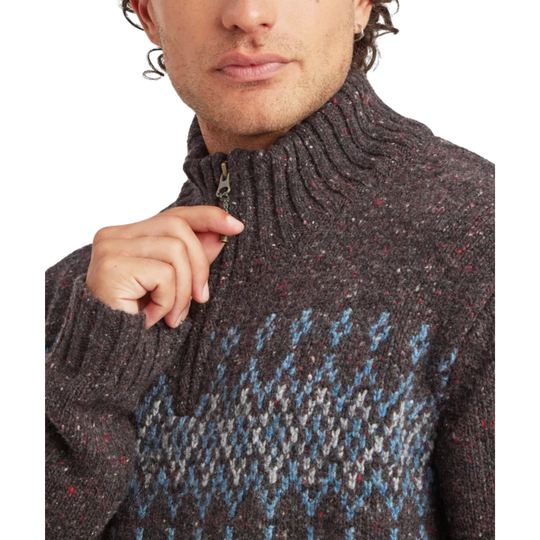 Close-up of a man wearing a dark brown knit quarter-zip sweater with a blue, gray, and white geometric pattern across the chest.