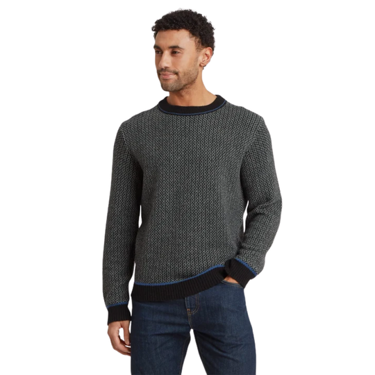 A man wearing a dark gray and black textured knit crewneck sweater with ribbed trim, paired with blue jeans, photographed against a solid white background.