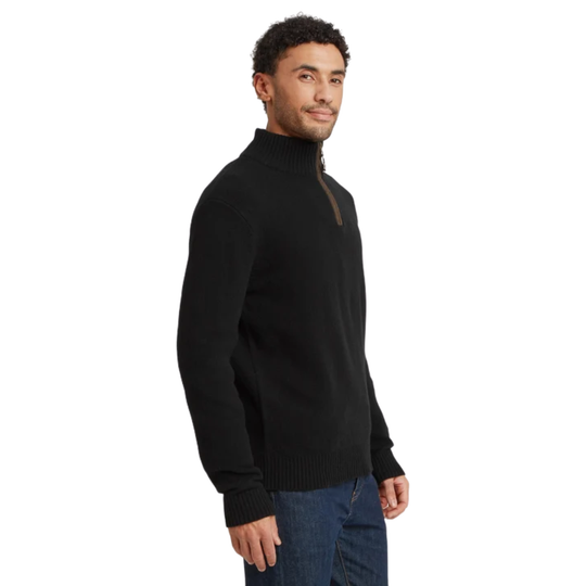 A man wearing a black ribbed mock neck quarter-zip sweater with a brown zipper pull, paired with blue jeans, shown from a side profile against a white background.