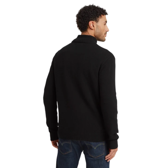 A man wearing a black ribbed mock neck quarter-zip sweater with a brown zipper pull, paired with blue jeans, shown from a back profile against a white background.