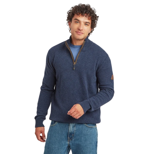 A man wearing a navy blue quarter-zip knit sweater over a blue t-shirt and blue jeans, standing against a solid white background.