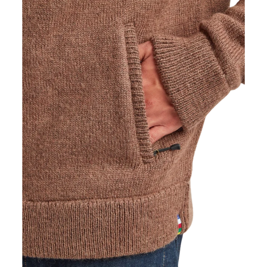 Close-up of a brown knit sweater with a side pocket, showing a hand in the pocket and ribbed cuffs and hem.