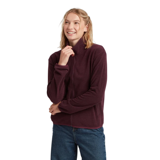 A woman wearing a dark burgundy zip-up fleece jacket and blue jeans, standing against a solid white background.