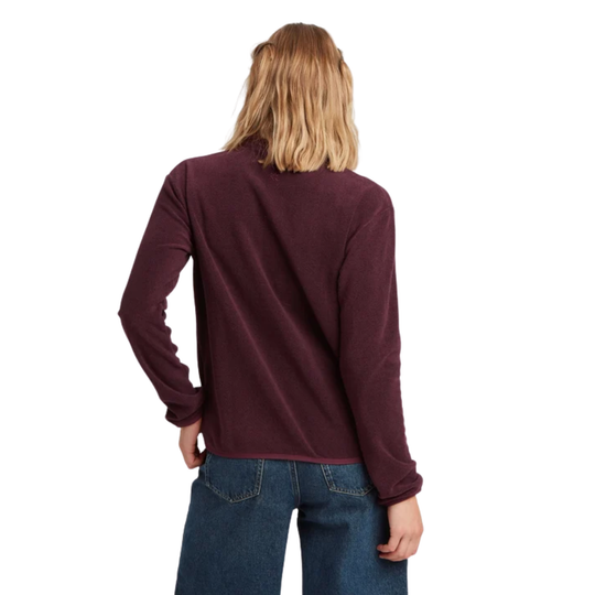 A woman with blonde hair is shown from the back wearing a long-sleeve fleece pullover in a deep burgundy color, paired with blue jeans, against a plain white background.