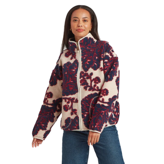 A woman wearing a quarter-zip fleece pullover with a bold floral pattern in navy blue and red on a cream background, paired with blue jeans, shown from a front profile against a white studio background.