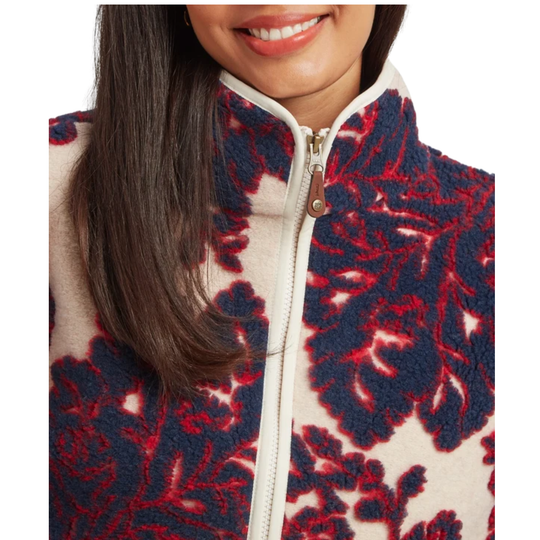 Close-up of a person wearing a textured fleece jacket with a bold navy blue and red floral damask pattern on a cream background.