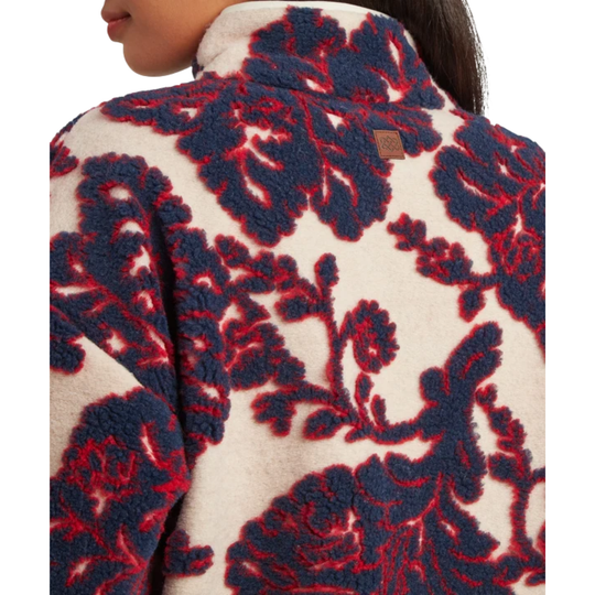 Close-up of a person wearing a textured fleece jacket with a bold navy blue and red floral damask pattern on a cream background.