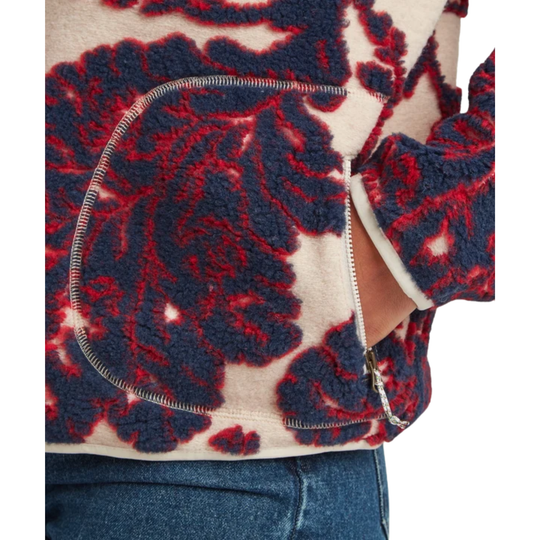 Close-up of a person wearing a textured fleece jacket with a bold navy blue and red floral damask pattern on a cream background.