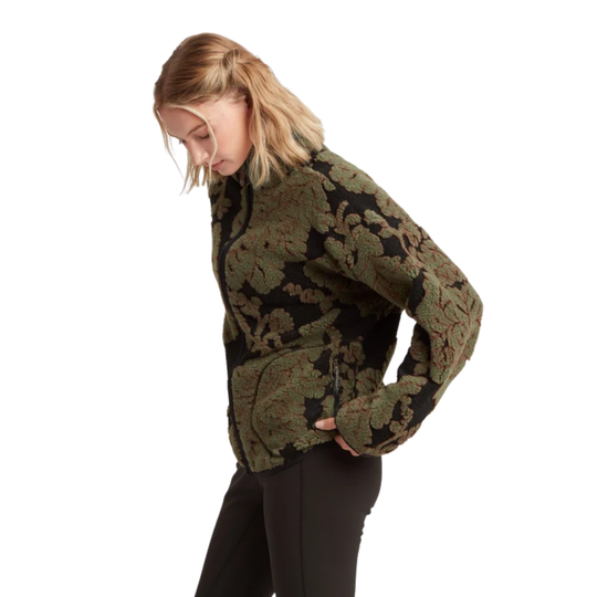 A woman shown from the side wearing a cropped, long-sleeve knit sweater with an intricate floral jacquard pattern in olive green and black, paired with black leggings, against a plain white background.