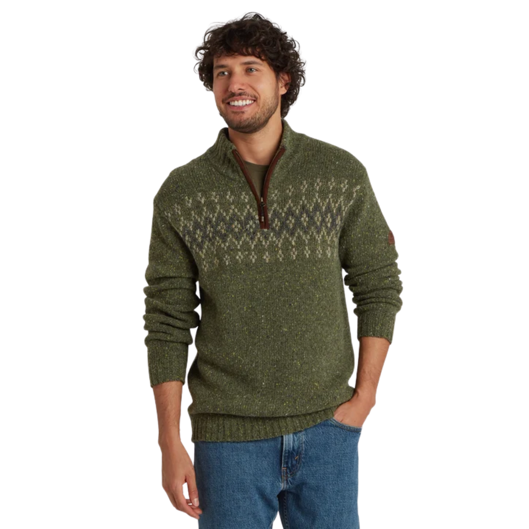 A man wearing a green knit quarter-zip sweater with a brown zipper and a beige geometric pattern across the chest, paired with blue jeans, set against a plain white background.