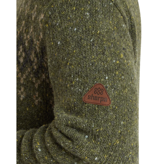 Close-up of a textured knit sweater sleeve in olive green with flecks of yellow, white, and brown, featuring a brown triangular Sherpa brand patch on the upper arm.