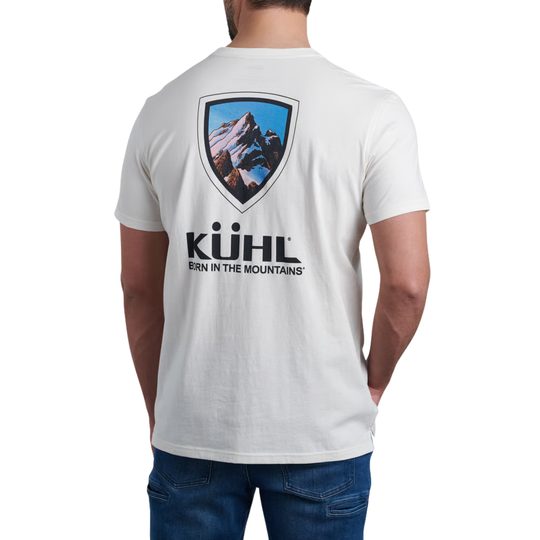 A man wearing a white short-sleeve t-shirt, viewed from the back. The shirt features a large graphic print on the back with a mountain shield logo and the text 'KÜHL BoRN IN THE MOUNTAINS'.
