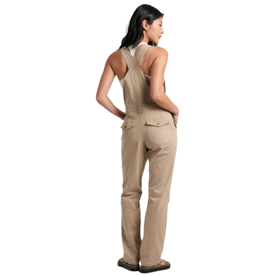 A woman modeling a pair of beige utility bib overalls, shown from a rear three-quarter angle against a solid white background.