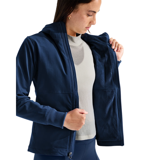 A woman wearing a navy blue zip-up hooded jacket over a light gray turtleneck sweater, shown from the waist up against a plain white background.