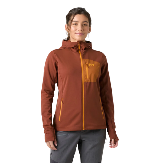 A woman modeling a rust-brown hooded jacket with a contrasting mustard yellow chest pocket and zipper details, paired with gray pants, against a plain white background.