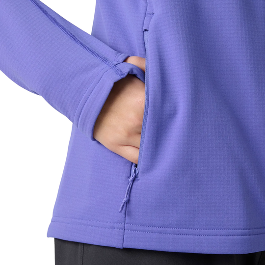 Close-up of a person wearing a purple long-sleeve athletic jacket, showing a side pocket with a hand inserted and a zipper closure.