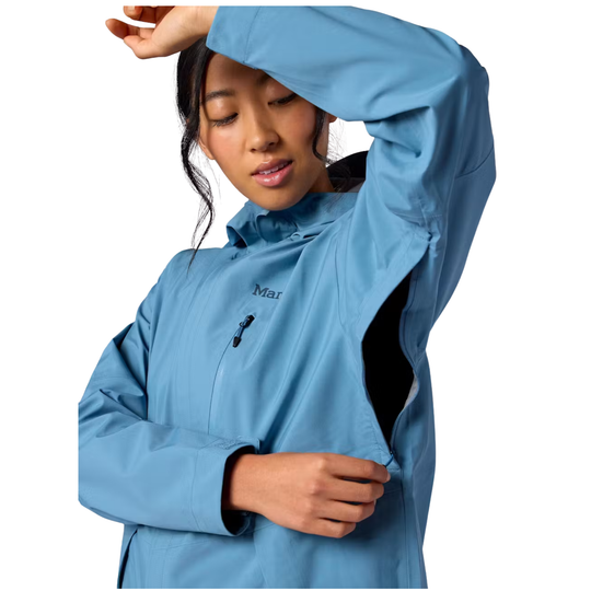 A woman wearing a light blue Mammo outdoor jacket, shown from the chest up against a plain white background. She is demonstrating the jacket's flexible, stretchable fabric on her upper arm and side pocket area.