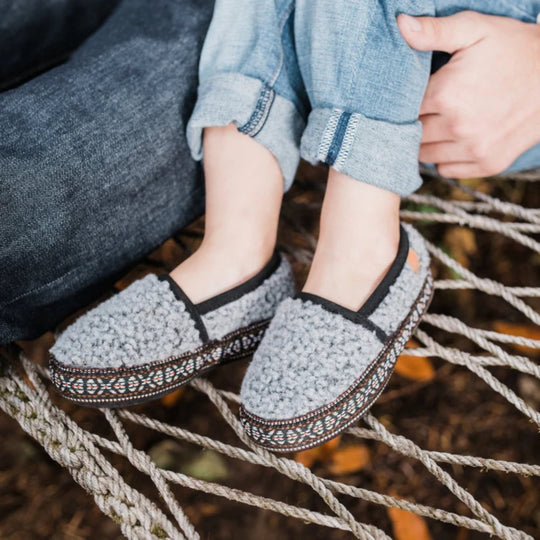 Gray fleece slip-on slippers with woven trim on a child’s feet