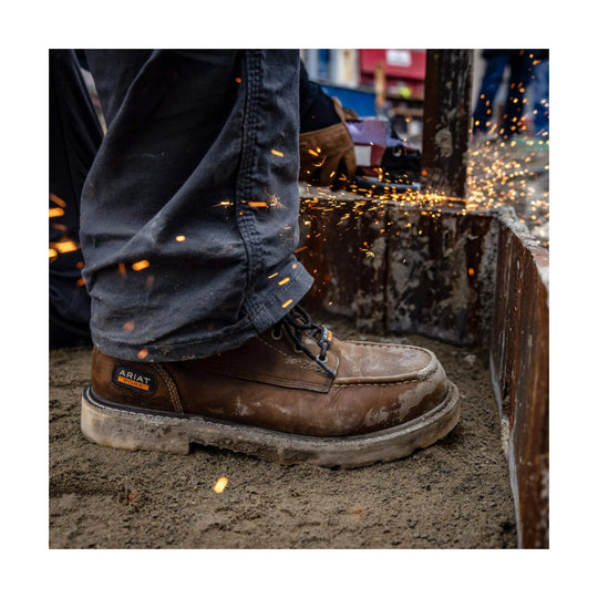 Brown leather work boot with black laces and a thick treaded sole, shown in use with dirt and sparks nearby