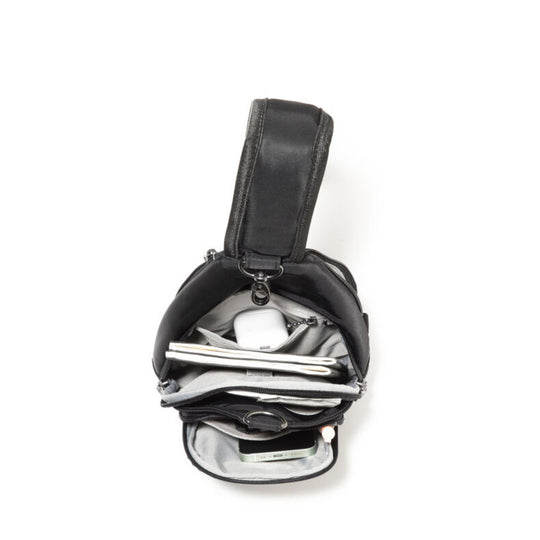 Black sling bag shown open with gray lining and multiple compartments, holding a notebook, earbuds, and a phone