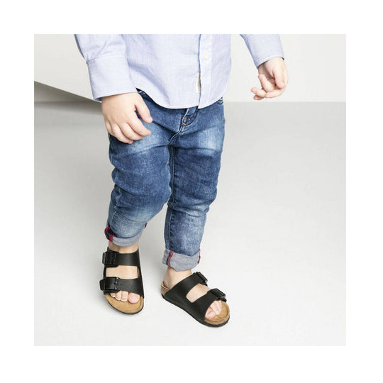 Black double-strap kids sandals on a child wearing rolled-up jeans