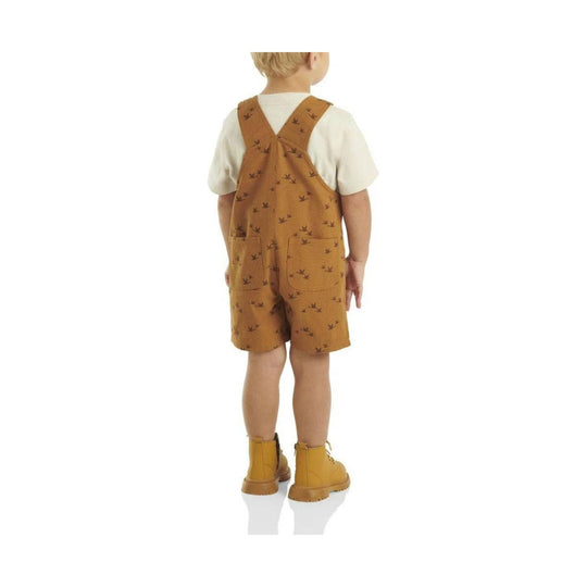 Toddler wearing brown printed short overalls over a white T-shirt and tan boots, back view