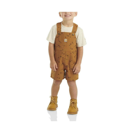 Toddler wearing a white T shirt with brown printed shortalls and tan lace-up boots