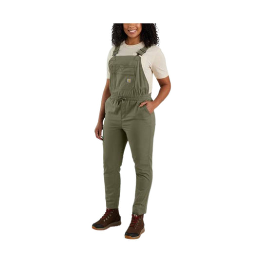 Woman wearing olive bib overalls over a cream T-shirt with front chest pocket and brown hiking boots