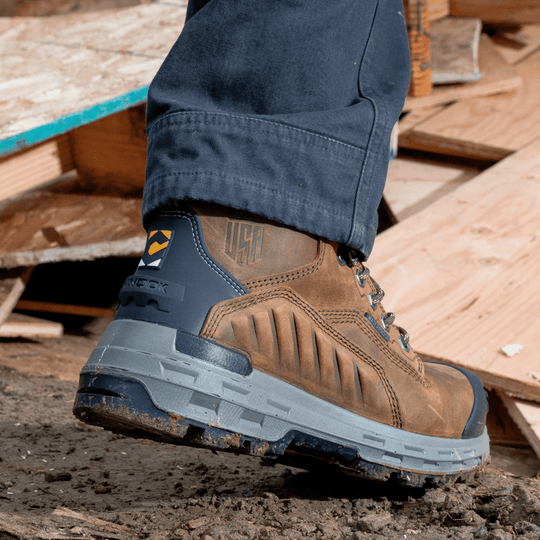 Brown and black waterproof work boot with gray lug sole, shown on a muddy jobsite