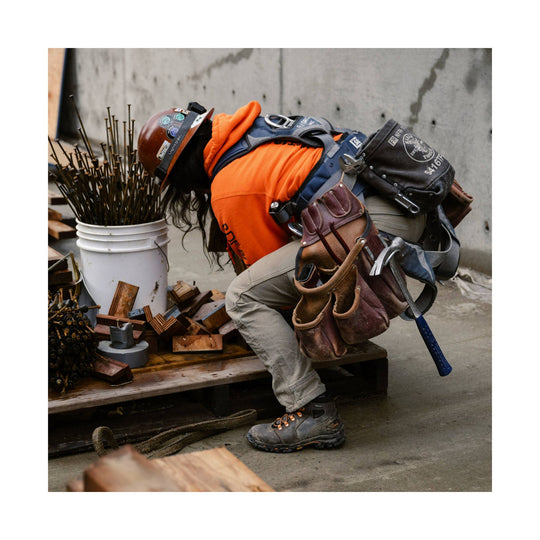 Brown and gray lace-up work boot on a worker wearing a harness and tool pouches